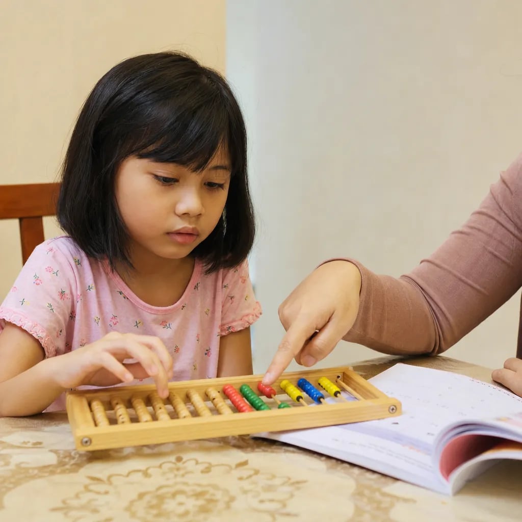 Malaysian girl aged 6 to 7 practising mental arithmetic on a wooden abacus at home with her mother